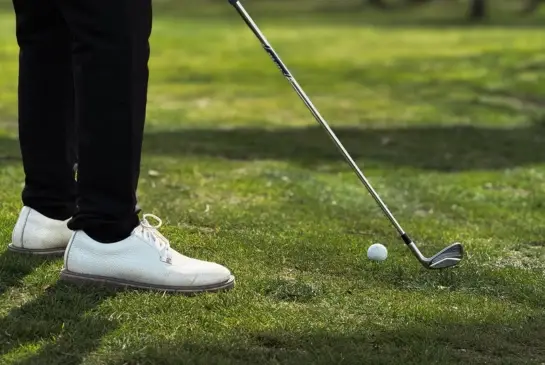 Close-up of a golfer's feet and iron club at address over a golf ball