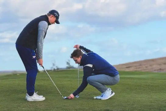 Alex Matthews checking a player's ball position and clubface alignment during a lesson at Whittington Heath Golf Club